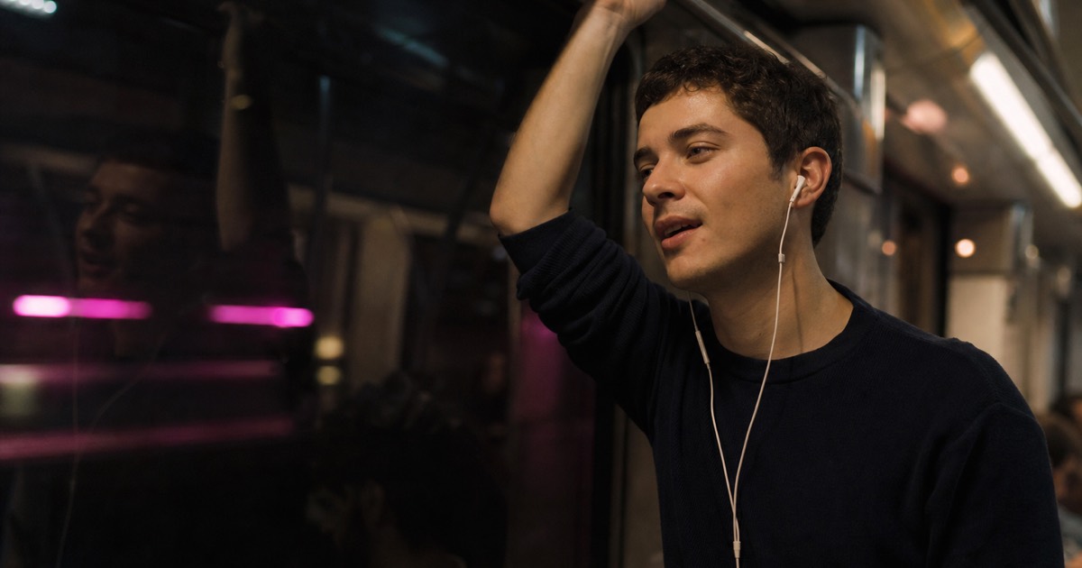 A commuter on an evening train, earbuds in, quietly repeating a Mandarin phrase to himself.